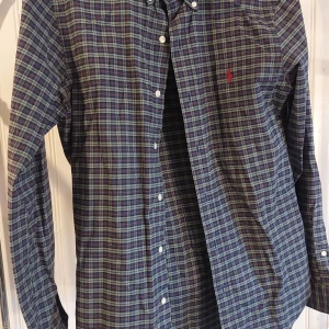 Rutig skjorta Polo Ralph Lauren S - Rutig långärmad skjorta från Polo Ralph Lauren i slim fit-modell. Skjortan har blå, gröna och röda toner, klassisk krage och knäppning framtill. Tillverkad i stretchig bomull för extra komfort. Ikonisk röd logga broderad på bröstet.