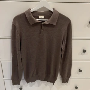 Brun långärmad pikétröja John Henric - Säljer en brun långärmad pikétröja från John Henric. Tröjan har klassisk krage, knäppning framtill och är tillverkad i merinoull som känns riktigt skönt mot huden. Perfekt för dig som gillar stilrena och enkla plagg.