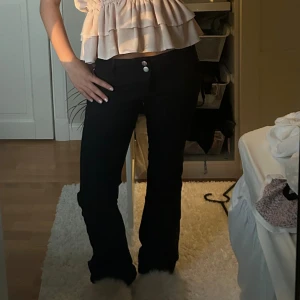 Svarta bootcut jeans med hög midja - Snygga svarta jeans med bootcut-snitt och två silverfärgade knappar i midjan. Låg midja och klassisk femficksdesign. Perfekta till sneakers eller boots för en chill och trendig look.