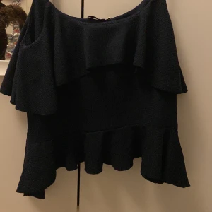 Blå volangtop från Nelly XS - Säljer en marinblå topp från Nelly i storlek XS. Toppen har smala axelband, ärmlös design och är dekorerad med dubbla volanger både upptill och nedtill. Materialet är ribbad syntet som ger en snygg struktur och lite glans. Perfekt för dig som gillar trendiga detaljer och volanger.