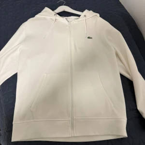 Vit hoodie från Lacoste med dragkedja - Lacoste hoodie med storlek L. Den är för stor för mig jag är 185cm och väger 79kg. Helt ny aldrig använd