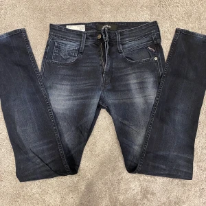 Replay Anbass Jeans - Säljer ett par mörkblå Replay Anbass jeans med snygg tvätt och diskreta slitningar. Modellen är skinny fit med smal passform och klassiska fem fickor. Jeansen har en modern look och är tillverkade i stretchig denim för extra komfort.