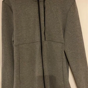Grå zip-hoodie med huva - Snygg grå hoodie med dragkedja och huva, perfekt för chill dagar. Jackan har långa ärmar, dragsko i huvan och en clean look utan synliga loggor. Materialet är mjukt och stretchigt, vilket gör den riktigt skön att bära.