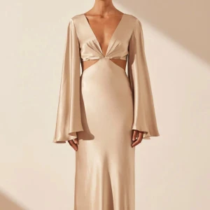 Shona Joy långklänning med öppen rygg - Säljer en elegant supervacker champagnefärgad långklänning med djup v-ringning och vida, långa ärmar. Den är från märket Shona Joy, och klänningen har snygga cut-outs vid midjan och en öppen rygg med knytband. Materialet är glansigt och känns lyxigt mot huden, perfekt för dig som vill sticka ut. Mycket mycket bra kvalitet! Endast använd en gång från föregående person då jag köpte den från Plick. Jag säljer den då jag hittat en annan. (Finns inga spår av användning)❤️. Nypris 5000 kr