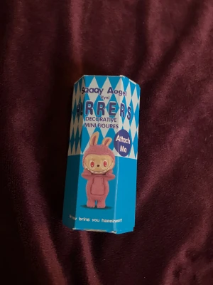 Rosa dekorativ mini figur Sonny Angel/ labubu  - Säljer en söt dekorativ mini figur från Sonny Angel, klädd i en fluffig rosa dräkt med kaninöron. Figurstilen är lekfull och unik med snurriga ögon och ett brett leende. Perfekt som samlarpryl eller dekoration till skrivbordet. Den går att fästa på en mobil eller dator. 