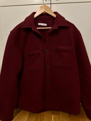 Vinröd Jacka från Zara |Man  - Snygg vinröd overshirt från Zara med två stora bröstfickor och knappar framtill. Jackan har klassisk krage och är tillverkad i mjukt ullmaterial. Perfekt för lager-på-lager och har en loose passform som ger en chill vibe.