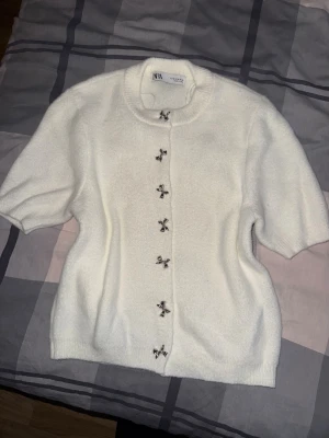 Vit kofta med rosettknappar från Zara - Superfin vit kofta från Zara med korta ärmar och unika silvriga rosettformade knappar framtill. Mjuk och fluffig känsla, använd 1 gång