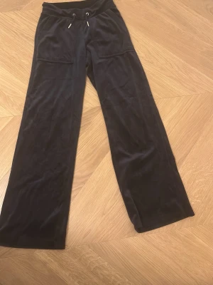 Svarta/mörk blåa mjukisbyxor från 157. - Svarta mjukisbyxor från 157. med breda ben och snörning i midjan. Byxorna har både fram- och bakfickor och är gjorda i ett mjukt, sammetsliknande material som känns riktigt skönt. Perfekta för chill dagar eller när du vill vara extra bekväm.