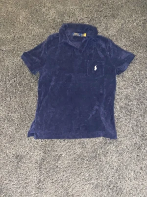 Mörkblå frotté piké från Polo Ralph Lauren - Säljer en mörkblå polopike från Polo Ralph Lauren i mjuk frotté. Piken har korta ärmar, klassisk krage och en bröstficka med broderad logga i vitt. Perfekt för dig som gillar lite mer stil. Storlek S. 500kr. I princip   helt oanvänd. Pris kan diskuteras 