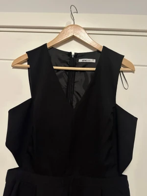 Svart jumpsuit från Gina Tricot - Säljer en svart byxdress från Gina Tricot i storlek 38. Byxdressen har v-ringad hals, breda axelpartier och dragkedja bak. Materialet är slätt och har en elegant look, perfekt för dig som gillar stilrena plagg med lite edge.