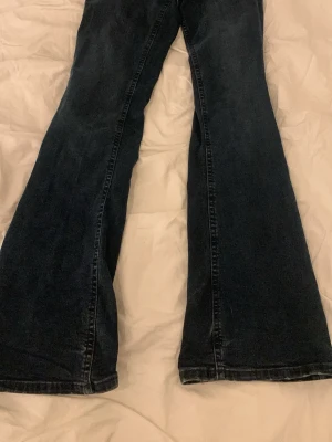 Bootcut jeans i mörkblå denim - Snygga bootcut jeans i mörkblå denim med klassisk femficksdesign. Jeansen har en bredare benslut som ger en cool siluett och är tillverkade i slitstarkt jeansmaterial. Perfekta för dig som gillar retrovibbar och vill sticka ut lite extra.