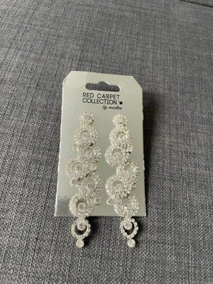Ingen väst på bilderna - Bilderna visar ett par glittriga örhängen från Red Carpet Collection by Montini, men ingen väst finns med.