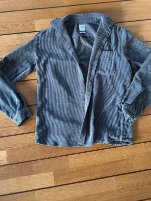 Grå manchester overshirt från Zara - Säljer en chill grå overshirt från Zara i mjuk manchester med relaxed fit. Skjortan har långa ärmar, knappar framtill och en bröstficka. Perfekt att slänga på över en t-shirt för en laidback vibe.