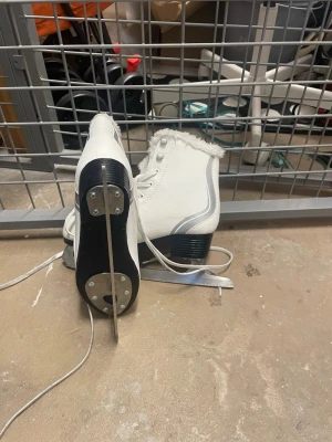 Vita skridskor från Spin med päls - Säljer ett par vita skridskor från Spin med fluffig päls runt skaftet och silvriga detaljer på sidan. Skorna har snörning och en robust klack, samt en platt sula med fastmonterad stålskena. Perfekt för dig som vill glida fram på isen med stil.