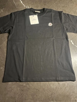 Svart Moncler t-shirt i bomull - Svart t-shirt från Moncler med klassisk rund hals och korta ärmar. T-shirten har Moncler-logga broderad på bröstet och är tillverkad i mjuk bomull. Enkel och stilren design som funkar till många olika looks. Perfekt för dig som gillar exklusiva märken.