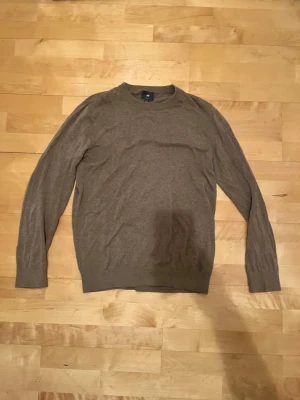 Brun slim fit tröja från H&M - Säljer en brun långärmad tröja från H&M i slim fit-modell. Tröjan har rund hals och ribbade muddar vid ärmslut och nederkant. Materialet är mjukt och lätt, perfekt för lager-på-lager under hösten eller vintern. Enkel och stilren design som funkar till många outfits.