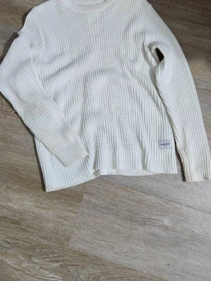 Vit stickad tröja från Jack & Jones - Säljer en vit stickad tröja från Jack & Jones Core med rund hals och långärmad design. Tröjan har ett snyggt strukturerat mönster med ribbade detaljer och är tillverkad i mjuk bomull. Perfekt för dig som gillar stilrena och bekväma plagg.