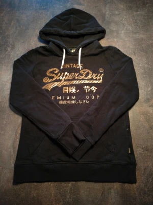 Superdry Hoddie  - Väldigt bra skick saknar dock 2 tecken. Modellen på bilden är 175cm lång och väger 80kg. Passar liten S 