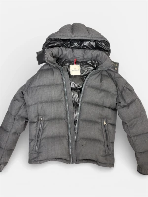  Moncler Montgenevre jacka. 2 - Säljer en mörkgrå pufferjacka från Moncler med huva och snygga detaljer som fickor med dragkedja och logotyp på ärmen.  Perfekt för kalla dagar och malla till sig med. Kvitto medföljs! Nypris på en montgenevre ca 20 000:- säljer billigt pga lite slitage vid ärmänden samt att moncler dragkedjan saknas men går att ersätta och beställa ny dragkedja (den fungerar perfekt redan) lite slitage på kragen men inget som syns. Pris kan diskuteras i DM. PRIS KAN DISKUTERAS VID SMIDIG AFFÄR🍾