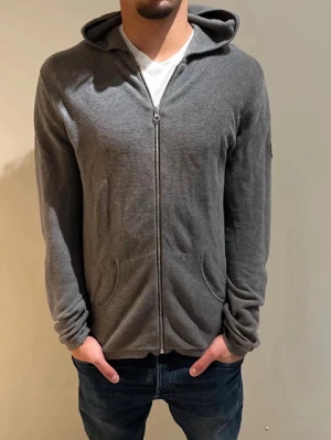 Grå cardigan/tröja från Ljung by Marcus Larsson - Säljer en stilren grå hoodie från Ljung Marcus Larsson i storlek M. Tröjan har dragkedja framtill, huva och två fickor. Materialet är mjukt och stickat, perfekt för chill dagar. Passformen är normal och ärmarna är långa. NYPRIS:1699Kr Mitt pris:349Kr ✅