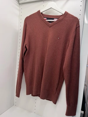 Brun tröja  Tommy Hilfiger - Snygg brun v-ringad tröja från Tommy Hilfiger med diskret logga på bröstet. Tröjan är långärmad och har ribbade muddar vid ärmslut och nederkant. Tillverkad i mjuk bomull, perfekt för dig som gillar klassisk stil med en modern touch. Den är bara använd en gång och är 92% bomull och 8% chasmire. Skriv ifall ni har frågor. 