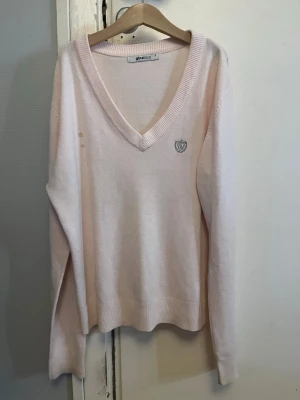 Ljusrosa v-ringad tröja Gina Tricot - Ljusrosa v-ringad tröja från Gina Tricot med lång ärm och ribbade muddar. Diskret broderad logga på bröstet. Mjuk och tunn stickad kvalitet som är perfekt för lager-på-lager. Enkel och stilren design som funkar till många olika looks.