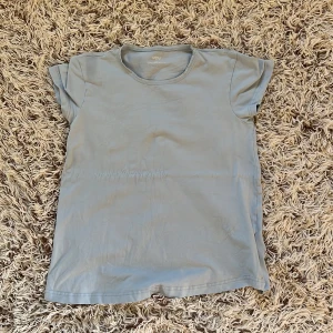 Ljusblå t-shirt från MOM by Lindex - Ljusblå t-shirt från MOM by Lindex i mjuk bomull med lite stretch. Klassisk rund hals och korta ärmar, perfekt för en chill och enkel look. Materialet är 95% bomull och 5% elastan, vilket gör den skön och följsam. Snygg att matcha med jeans eller shorts.  Perfekt till sommaren. Storlek EUR 34