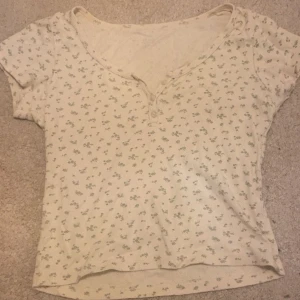 Blommig ribbad topp med knappar - Såå söt ljusbeige ribbad topp med små gröna blommor, köpt 2023 men inte använd på lång tid