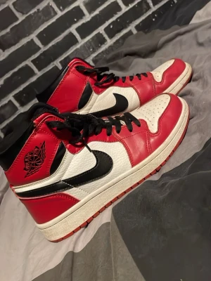 Nike Air Jordan 1 High Chicago strl 40 - Säljer ett par Nike Air Jordan 1 High Chicago med klassisk färgblockning i rött, vitt och svart. Skorna har snörning, rund tå och platt sula. Tillverkade i skinn med ikonisk Air Jordan-logga på sidan och svart swoosh. Perfekta för dig som vill ha en ikonisk sneaker med streetkänsla.