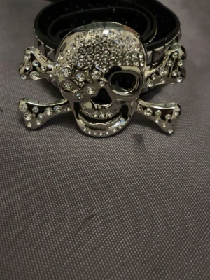 Y2K Skelettbälte – Edgy Goth / Punk Statement Accessoar - ✨ Statement-bälte som lyfter hela outfiten   Snyggt och edgy bälte med ett iögonfallande glittrigt skelettspänne som ger direkt attitude till din look. Perfekt för dig som vill sticka ut – funkar lika bra till jeans som till kjol eller shorts. Ett riktigt statement-piece som gör det lilla extra, både till vardags och fest.  Detaljer: • Unikt skelettspänne med glitter • Trendig, edgy & unisex design • Längd: ca 100 cm • Skick: som ny • Färg: Vit  📦 Redo att skickas – hör av dig vid frågor 🖤 Finns