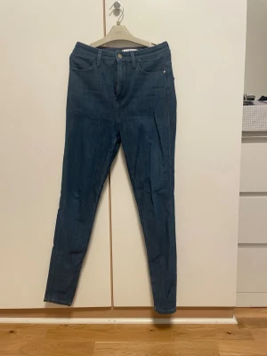 Tommy Hilfiger Ultra Skinny Jeans W27 - Snygga blå Ultra Skinny Ankle jeans från Tommy Hilfiger. Modellen är skulpturformad med smal passform hela vägen ner till ankeln. Klassisk femficksdesign, med logga på bakfickan och läderpatch i midjan. Materialet är stretchigt jeans i bomull och polyester.
