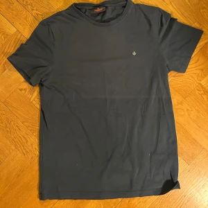 Svart t-shirt från Morris Stockholm - En stilren mörkblå t-shirt från Morris med liten broderad logga på bröstet. Klassisk passform, rund hals och korta ärmar. Bekväm och stretchigt tyg och tight runt ärmarna.
