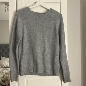 Grå stickad tröja från Vero Moda - En enkel och stilren grå stickad tröja från Vero Moda. Tröjan har rund halsringning, långa ärmar och ribbade muddar vid ärmslut och nederkant. Perfekt att slänga på sig när det är kyligt ute.