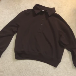 Brun tröja med krage och knappar   - Mörkbrun tröja i mjukt material med klassisk krage och knappar framtill. Tröjan har långa ärmar och bred mudd vid midjan för en snygg passform. Perfekt för dig som gillar stilrena och enkla plagg. Och passar perfekt nu till hösten med både Stilen men också färgen. (Priset diskuteras)