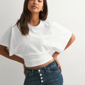 Vit croppad topp med vida ärmar - Säljer en vit croppad topp med rund hals och vida, korta ärmar. Toppen har en tight passform över midjan och är tillverkad i mjuk bomull. Perfekt för dig som gillar en clean och stilren look.