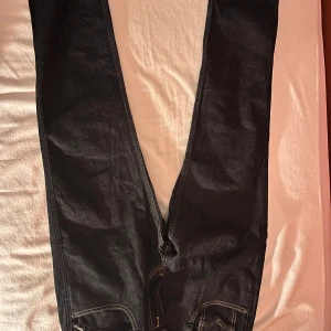 Replay Anbass mörkblå jeans 34 - Snygga mörkblå Replay Anbass jeans med klassisk femficksdesign och kontrastsömmar. Jeansen har raka ben och tydliga detaljer som Replay-logga på bakfickan och läderpatch i midjan. Perfekta för dig som gillar stilrena och tidlösa jeans. Dom är helt nya har inte använts