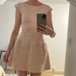 Maje miniklänning, storlek 1 - Supersöt ljusbeige kortklänning från Maje med snygga hålmönster i geometriska linjer på överdelen och en ribbad, lätt utställd kjol. Klänningen har korta ärmar och rund halsringning, perfekt för dig som gillar stilrena detaljer och feminin siluett. Storlek 1 vilket motsvarar storlek XS/S