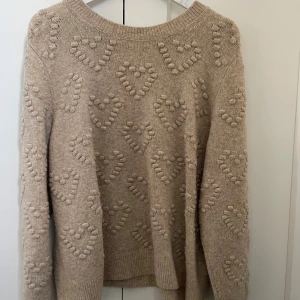 Beige stickad tröja med hjärtmönster - Supermysig beige stickad tröja med upphöjda hjärtan över hela. Tröjan har rund halsringning, ribbade muddar och långa ärmar. Matrialet sticks inte!!
