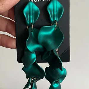 Turkosa statementörhängen från Monki - Unika och stora örhängen från Monki i en cool turkos färg. De har en vågig, organisk form som verkligen sticker ut och ger en modern vibe. Perfekta för dig som vill ha ett smycke som syns och känns trendigt.