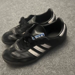 Adidas Samba svarta sneakers strl 45 - Klassiska Adidas Samba sneakers i svart skinn med vita ränder och svart sula. Ikonisk retrostil med snörning och låg profil. Perfekta för dig som gillar streetwear och sportig vibe. Märke och storlek syns tydligt på etiketten. Originalbox medföljer. Nypris 1300:-