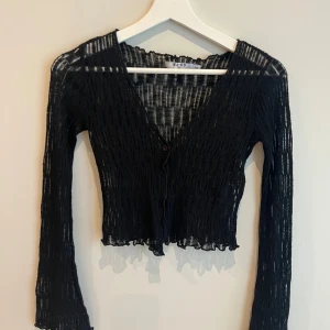 Finstickad svart cardigan från NA-KD - Finstickad svart cardigan från NA-KD med en knapp framtill. Kortare modell i stretchig kvalitet.