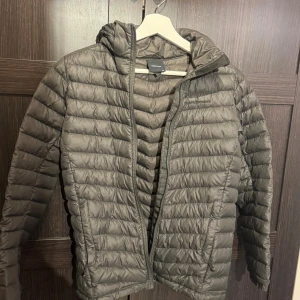 Grå dunjacka Peak Performance 160 - Säljer en grå dunjacka från Peak Performance i storlek 160. Jackan har huva, horisontella sömmar och dragkedja framtill. Perfekt för kyliga dagar och riktigt lätt att bära. Klassisk och stilren design som funkar till det mesta.