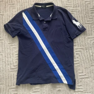 Blå Polo Ralph Lauren t-shirt - Snygg mörkblå t-shirt från Polo Ralph Lauren i bomull med klassisk pikékrage. Har blå och vit diagonal rand på framsidan och stor vit broderad polospelare på ärmen. Perfekt för dig som gillar sportig och stilren look. Storlek XL barn, Som passar Herr S,köp gärna bundle för skööön rabatt!  vid fler frågor eller funderingar tveka inte på att skriva🤝🏼