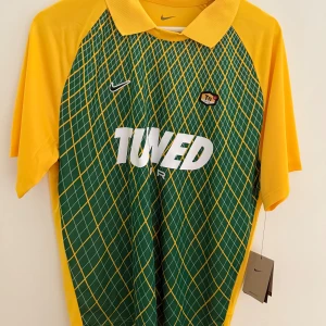 Unik Nike TN T-shirt - Nike Dri-FIT fotbollströja i loose fit med grön och gul rutig framsida, gula ärmar och krage. Stort 'TUNED AIR'-tryck på bröstet och Tn Air-märke. Tillverkad i lätt, ventilerande polyester för maximal komfort på planen.