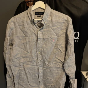 Ljusgrå linneskjorta från Ralph Lauren - Säljer en stilren ljusgrå skjorta från Ralph Lauren i klassisk passform. Skjortan är tillverkad i linne, har långa ärmar, knappar framtill och en liten broderad logga på bröstet. Perfekt för dig som gillar en clean och avslappnad look.
