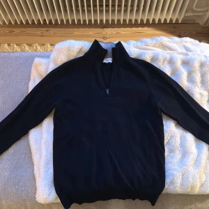 Mörkblå kashmirtröja från Davida - Snygg mörkblå stickad tröja från Davida i 100% kashmir. Tröjan har lång ärm, hög krage och en half zip-dragkedja framtill. Perfekt för dig som gillar stilrena och lyxiga basplagg med en mjuk känsla.