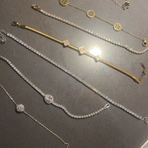   armband  - Flera snygga armband i både guld och silver, vissa med gnistrande stenar och andra med dekorativa berlocker och fyrklöverdetaljer. Perfekt för att mixa och matcha till din stil. Några armband har glittriga stenar och andra har eleganta gulddetaljer.