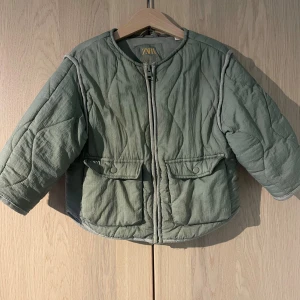 Grön quiltad jacka från Zara - Säljer en ljusgrön quiltad jacka från Zara i storlek 3-4 år. Jackan har rund hals, dragkedja framtill och två stora fickor med lock. Den är lätt vadderad och har en loose passform med långärmade ärmar. Perfekt för kyliga dagar!