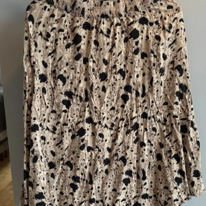 Beige och svart mönstrad kjol från Object - Säljer en beige kjol från Object med svart abstrakt mönster. Kjolen har resår i midjan och är tillverkad i ett lätt och luftigt material som passar perfekt för varmare dagar. Snyggt flowy fall och midilängd som ger en avslappnad men trendig look.