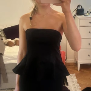 Svart bandeau topp från Zara - Snygg svart bandeau topp från Zara med volang nertill. Toppen är axelbandslös och har en figurnära passform upptill som släpper ut i en veckad peplum-liknande volang. Materialet är mocka. Storlek S. Aldrig använd, prislapp kvar. Säljer för 200, pris går att diskutera. 